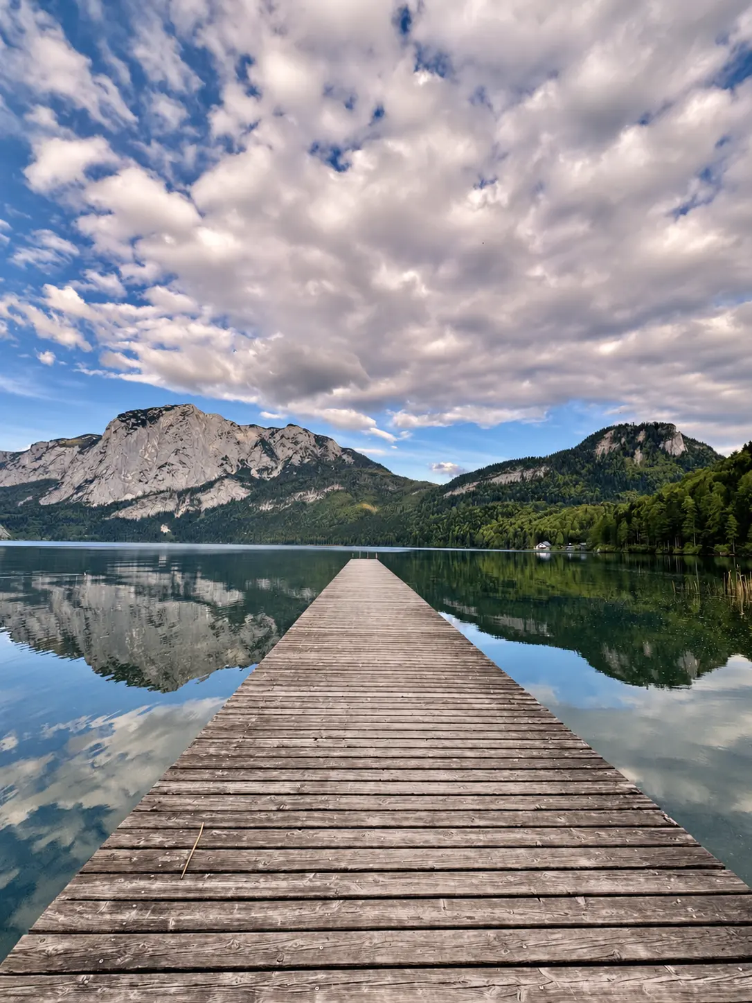 Holzsteg über einem ruhigen Bergsee mit Blick auf bewaldete Berge